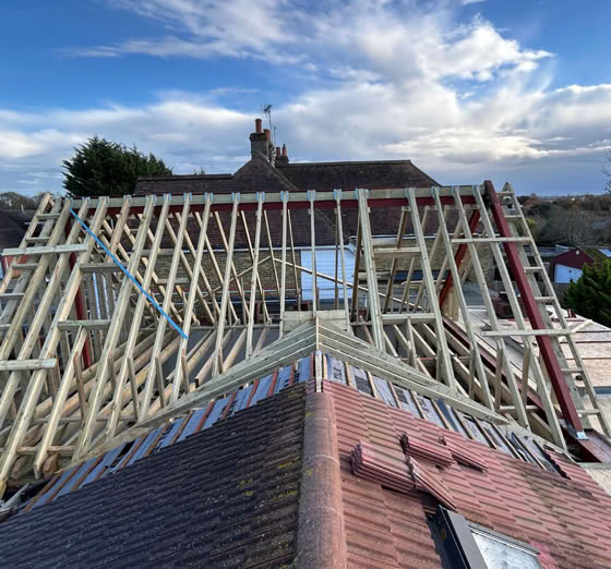 A rooftop under construction with wooden beams exposed, set against a partly cloudy sky.