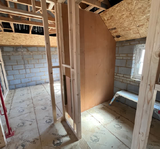 Interior of a partially constructed building with exposed wooden framing, concrete block walls, and a window.