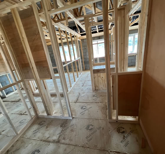 Interior view of a building under construction, showing wooden framing, exposed beams, and unfinished walls and floors.