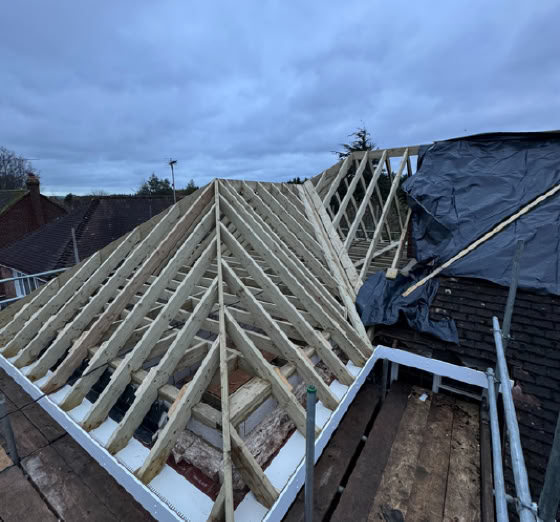Wooden roof trusses under construction on a building, with a cloudy sky in the background.