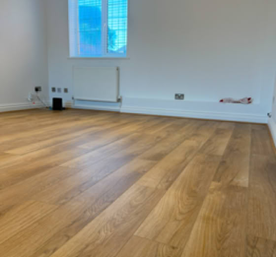 Empty room with wooden flooring, white walls, a window with a grid pattern, and a radiator beneath the window.