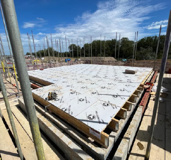 Construction site with a large concrete slab, surrounded by scaffolding and metal rods, under a blue sky with scattered clouds.