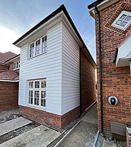 A narrow alley between two brick houses, with one house featuring white cladding and multiple windows.
