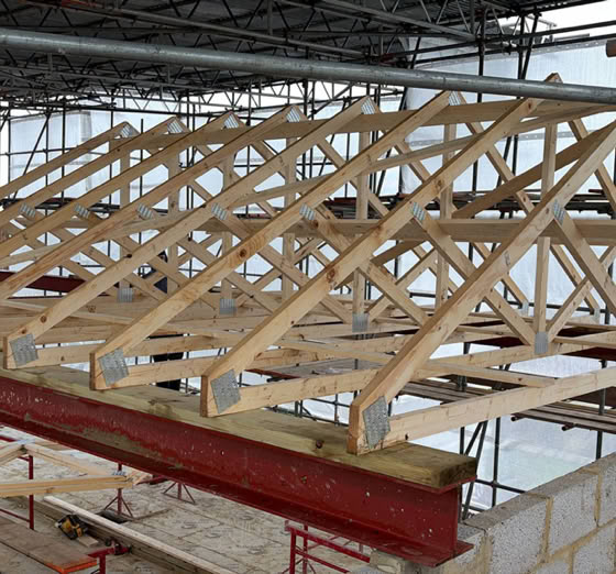 Wooden roof trusses under construction with scaffolding surrounding the structure.