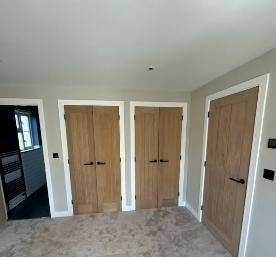 A room with three wooden doors, light-colored walls, and a carpeted floor.
